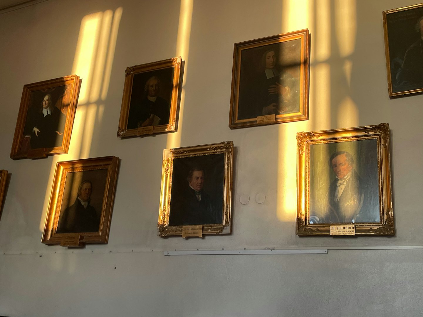Oude portretten in sierlijke lijsten hangen aan een zonnige muur.