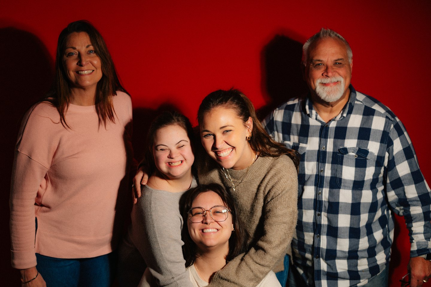 Een lachende, meergeneratie familie poseert samen voor een rode achtergrond.